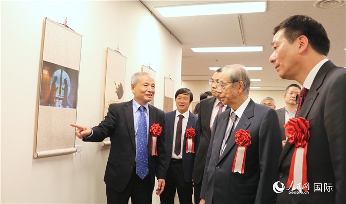 “湖州印象”攝影展主創(chuàng)、世界華人攝影協(xié)會副會長馮學敏向吳江浩大使、福田康夫前首相等嘉賓介紹展出作品。（人民網(wǎng) 許可攝）