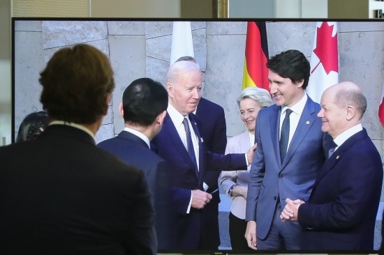 2022年3月24日，在比利時布魯塞爾的北約總部，一名男子觀看屏幕上美國總統(tǒng)拜登（右四）、歐盟委員會主席馮德萊恩（右三）、加拿大總理特魯多（右二）、德國總理朔爾茨（右一）出席七國集團(tuán)峰會合影儀式的畫面。新華社記者鄭煥松攝