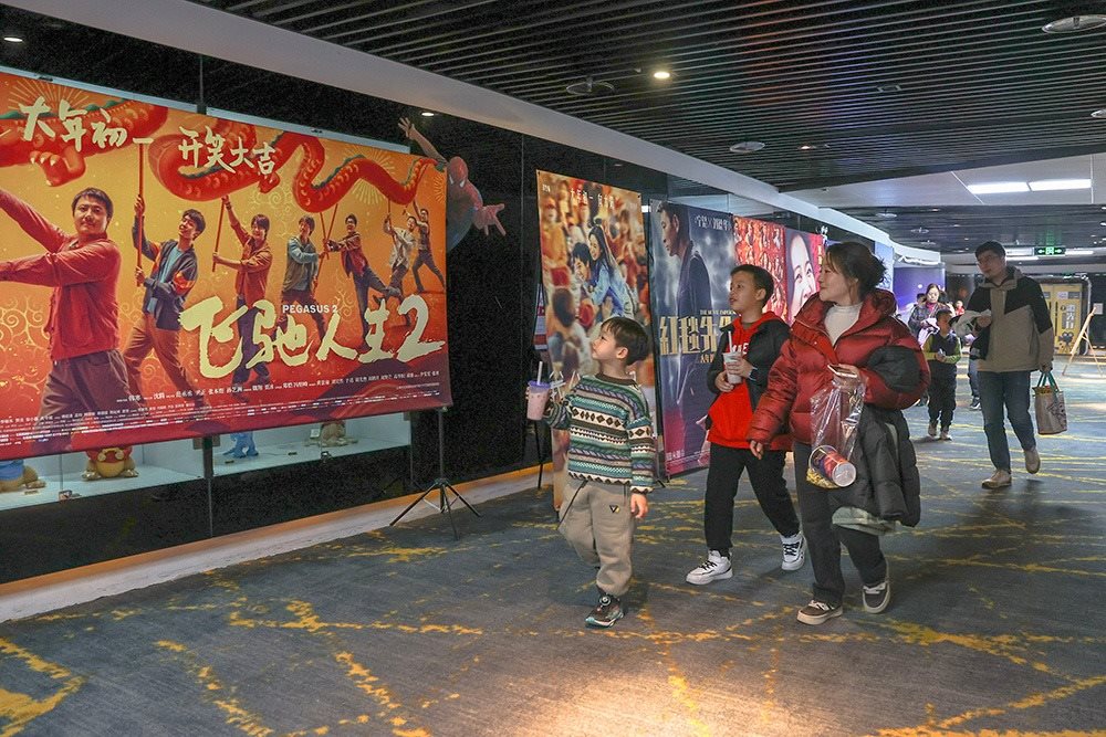 △ 2024年2月16日，在江西贛州一家電影院，觀眾從春節(jié)檔電影的宣傳展板前走過。