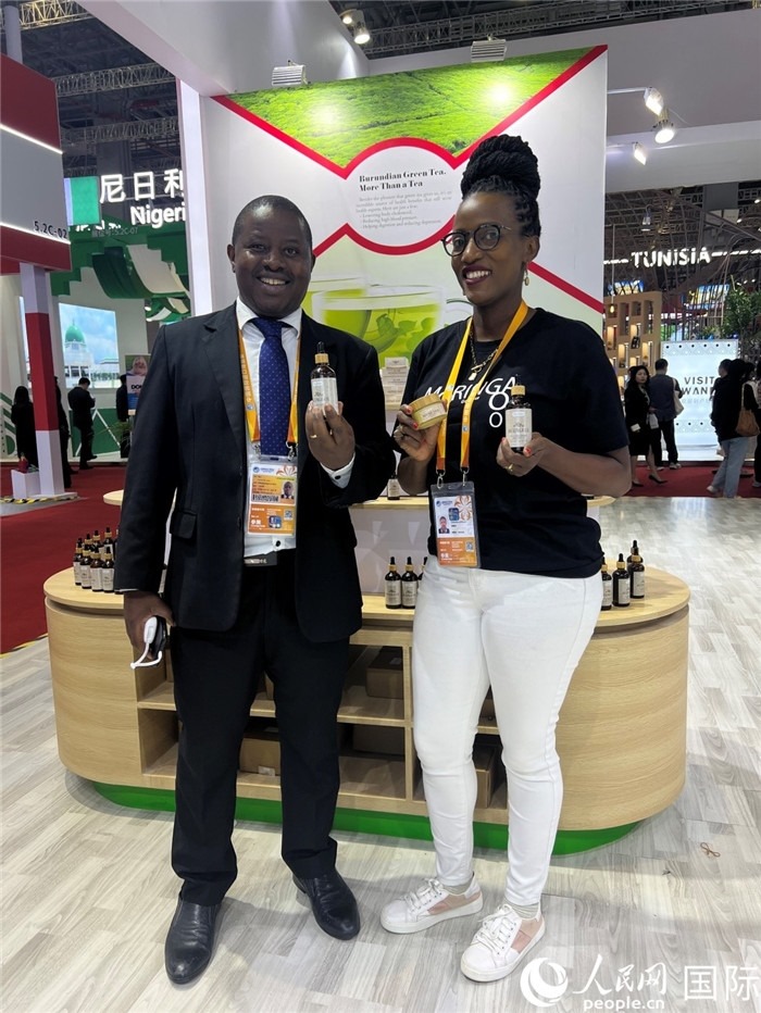 6月6日，布隆迪駐華大使館一等參贊布利馬索·阿爾弗雷德 (左，Bulimaso Alfred) 和參展商卡馬里扎·埃斯特拉 (Kamariza Estella) 在第七屆中國國際進(jìn)口博覽會布隆迪館展示當(dāng)?shù)厣a(chǎn)的辣木油。（人民網(wǎng) 艾里士 攝）